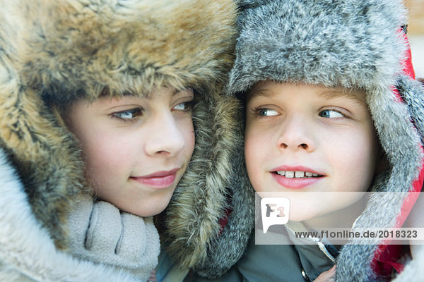 Sister and brother wearing fur caps  smiling at each other  portrait