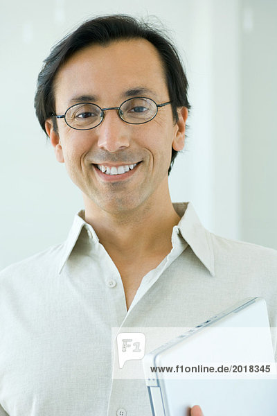 Man smiling at camera  holding laptop computer  portrait