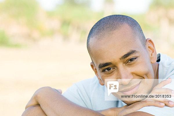 Man with shaved head  smiling at camera  head resting on arms  portrait