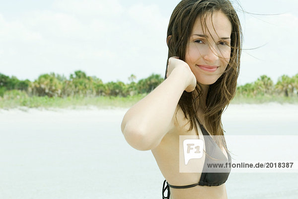 Junge Frau lächelt vor der Kamera  trägt Bikini  zerzaustes Haar  Portrait