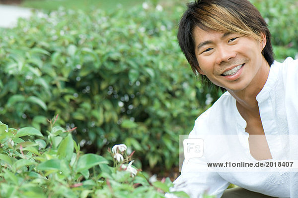 Man smiling at camera next to flowering shrub  portrait