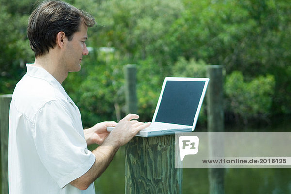 Man using laptop computer outdoors  next to lake