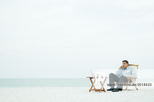 Man sitting in chair on the beach  looking at laptop computer  hand under chin