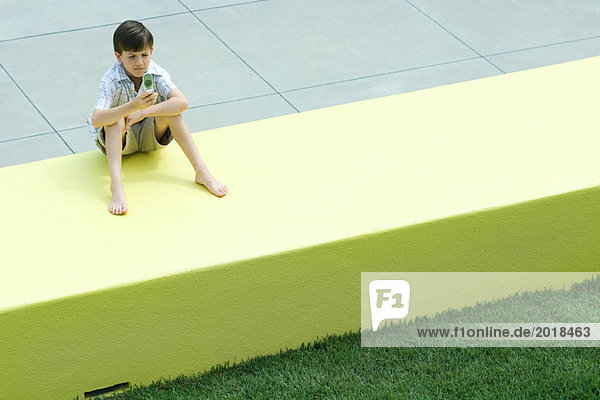 Boy sitting on low wall  looking at cell phone  squinting
