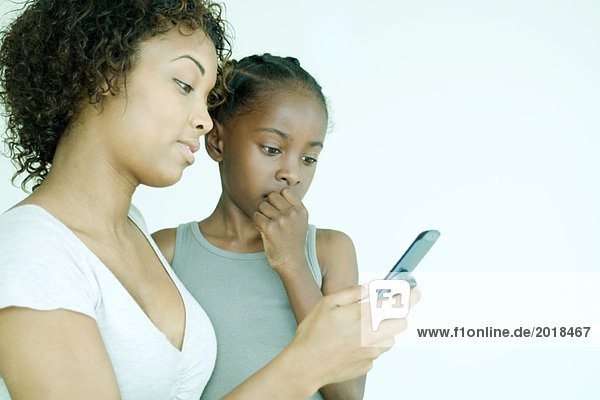 Mutter und Tochter schauen zusammen auf das Handy  die Hand des Mädchens über den Mund.