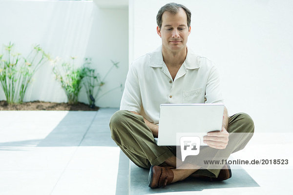 Man sitting on the ground using laptop computer  smiling  full length