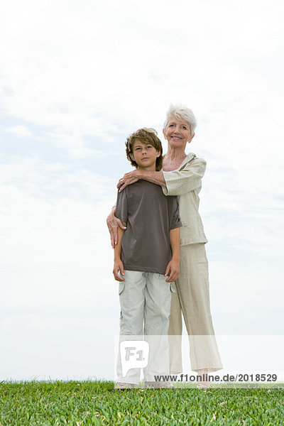 Seniorin und Enkelin  auf Rasen stehend  volle Länge