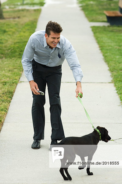 Man walking dog on sidewalk  bending forward  smiling