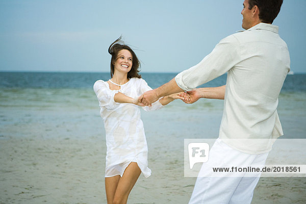 Mann und junge Begleiterin am Strand  Händchen haltend  sich gegenseitig schwingend