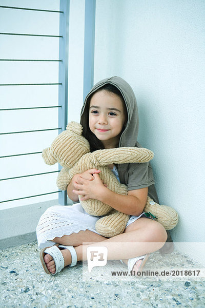 Kleines Mädchen auf dem Boden sitzend  Teddybär haltend  lächelnd  volle Länge