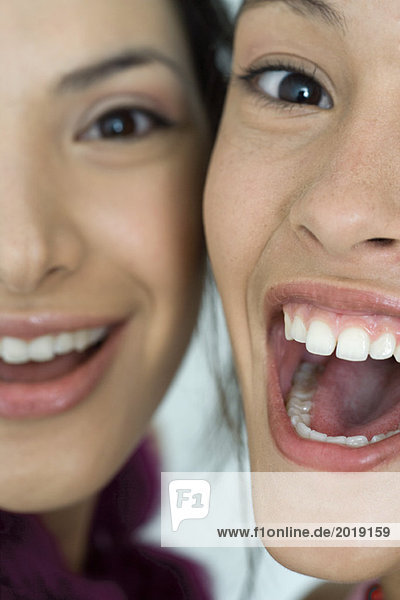 Zwei junge Freundinnen lächelnd mit weit geöffnetem Mund  Blick in die Kamera  extreme Nahaufnahme der Gesichter  beschnitten