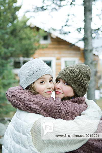 Two young friends embracing  dressed in winter clothing  looking over shoulders at camera  portrait