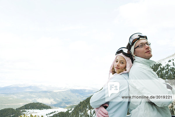 Young man and teen girl skiers standing back to back  smiling  girl looking at camera  portrait