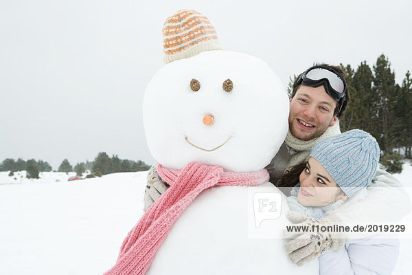 Two young friends standing with snowman  both smiling  one looking at camera