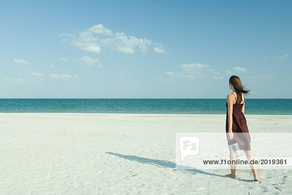 Frau geht über den Strand  trägt transparenten Behälter  volle Länge  Rückansicht