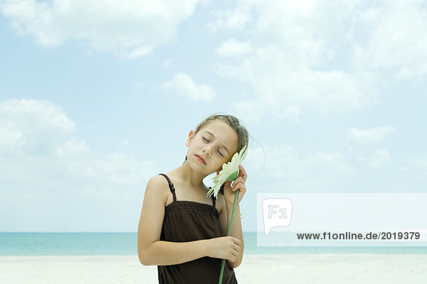 Mädchen steht am Strand  hält Blume am Ohr  Augen geschlossen  Taille oben