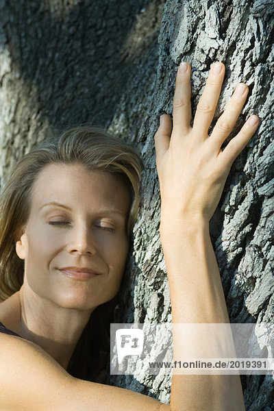 Frau umarmt Baum  Augen geschlossen  lächelnd  Kopf und Schultern