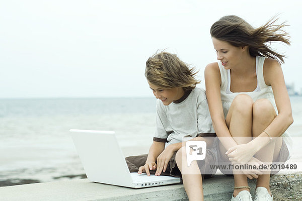 Teenager Mädchen und kleiner Bruder mit Laptop in Küstennähe