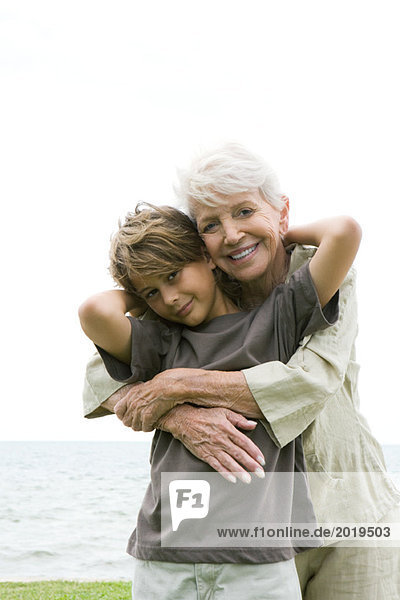 Seniorin umarmt Enkelin von hinten  beide lächelnd in die Kamera  Porträt