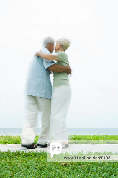 Senior couple dancing on sidewalk overlooking ocean  full length  blurred motion