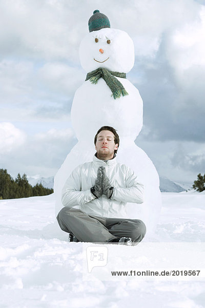 Junger Mann meditiert vor Schneemann