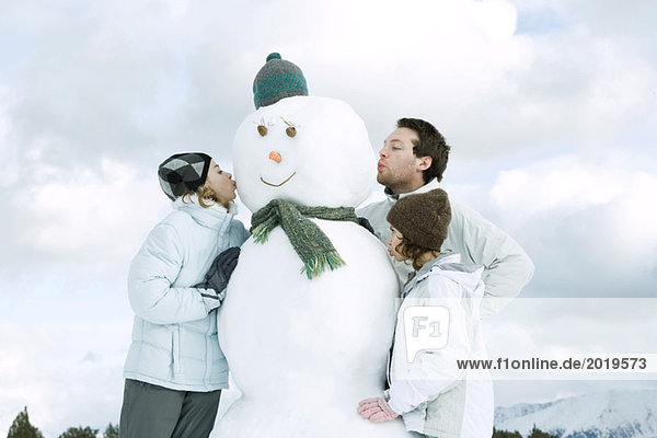 Three young friends kissing snowman