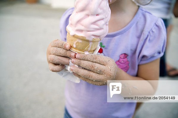 Young girl holding an ice cream with sand sticking to her hands