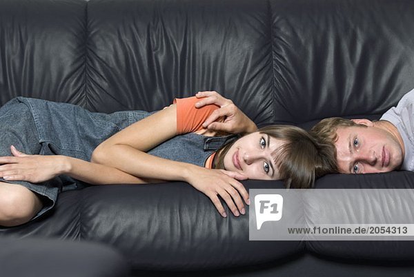 Eine junge Frau und ein junger Mann liegen auf einem Ledersofa.