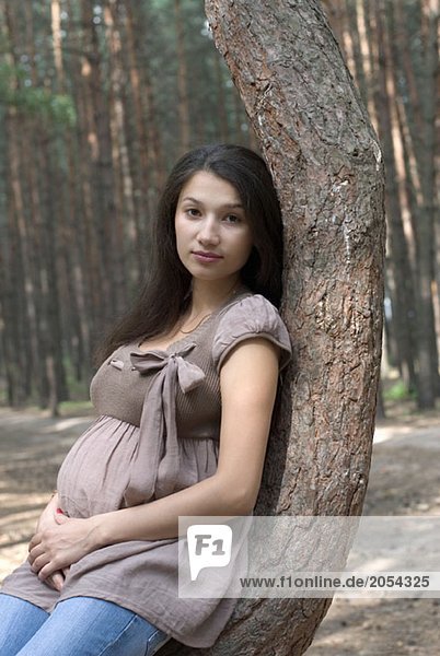 A pregnant woman leaning against a tree in the woods