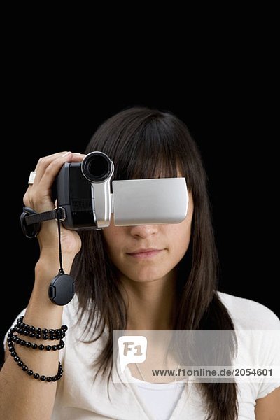 Eine junge Frau hält eine Videokamera vor ihr Gesicht.