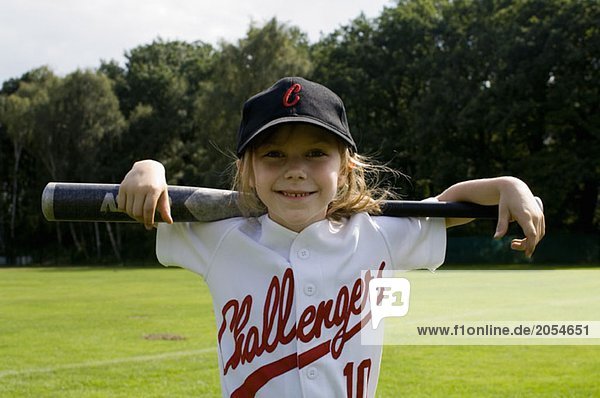 Ein junges Mädchen hält einen Baseballschläger auf ihren Schultern.