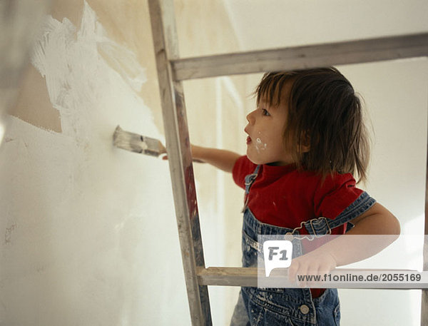 A young boy standing on a ladder and painting a wall