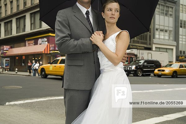 A bride and groom standing underneath an umbrella on a Manhattan street