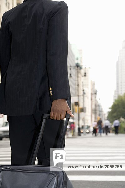 Businessperson rolling luggage down city street
