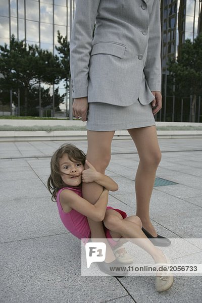 Ein kleines Mädchen umklammert das Bein einer Geschäftsfrau