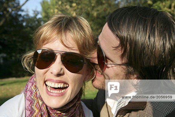 Ein Mann flüstert in das Ohr einer lachenden jungen Frau