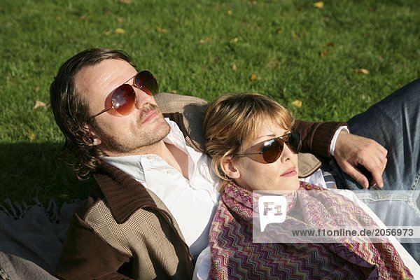 Ein junges Paar mit Sonnebrillen sonnt sich im Park