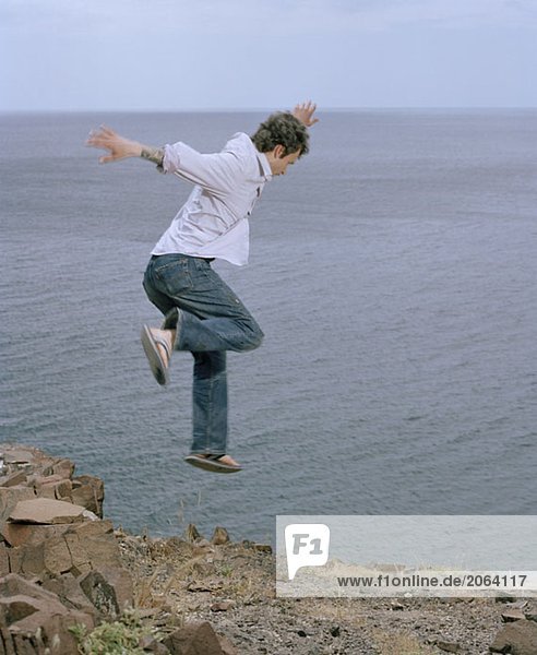 Ein Mann  der von einer Klippe in der Nähe des Meeres springt.