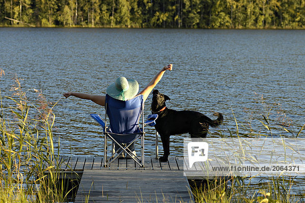 Rückansicht Frau sitzt in Sessel am Pier mit Hund