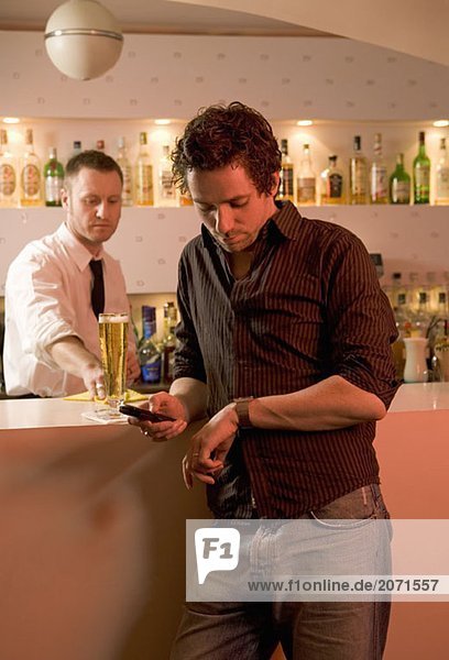 Ein Junger Mann wartet an der Bar mit dem Barkeeper im Hintergrund