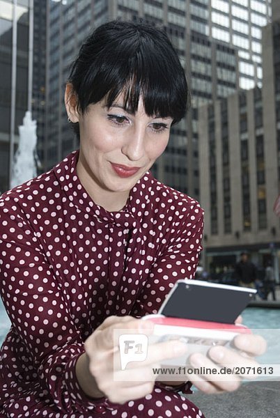 Junge Frau sitzt an einem Springbrunnen und verschickt SMS  New York City