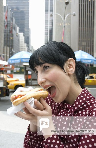 Junge Frau beißt auf der Straße stehend in ein Hotdog  New York City