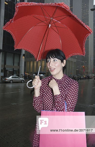 Junge Frau mit Regenschirm und Einkaufstaschen auf der Straße  New York City