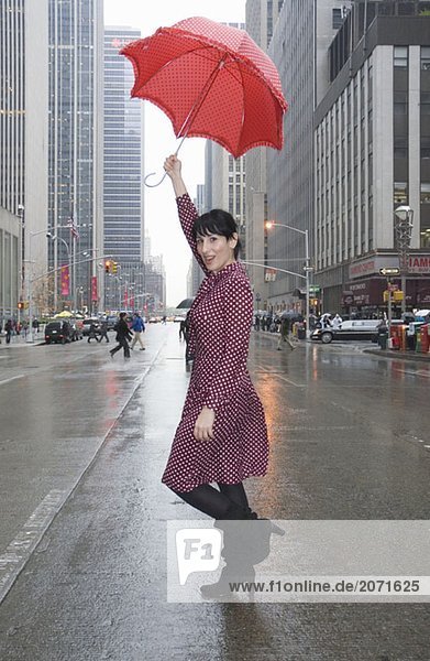 Junge Frau in einem gepunkteten Kleid und mit Regenschirm auf einer Straße  New York City