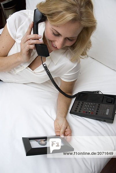 Eine Frau betrachtet eine Fotografie mit Kindern während sie auf dem Bett eines Hotelzimmers liegt und telefoniert