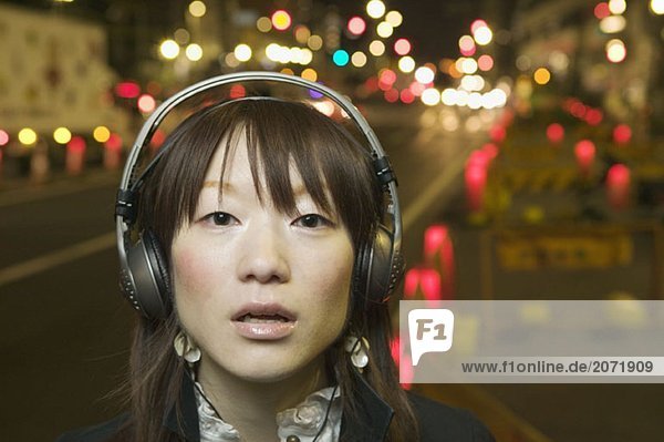 Eine junge Frau steht auf der Straße und hört Musik mit Kopfhörern  Tokio  Japan