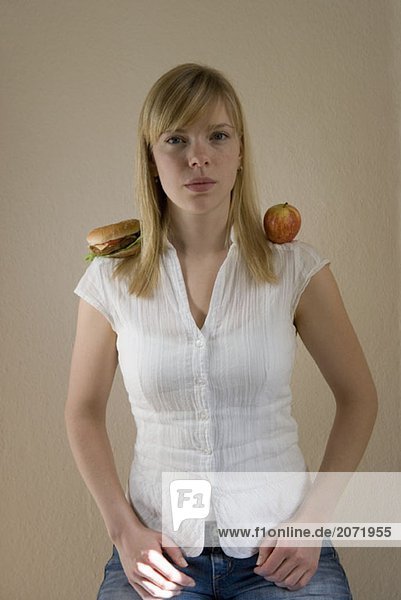 Eine junge Frau mit einem Apfel auf der einen und einem Hamburger auf der anderen Schulter
