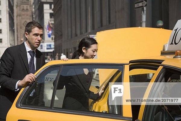 Ein Geschäftsmann und eine Geschäftsfrau steigen in ein gelbes Taxi