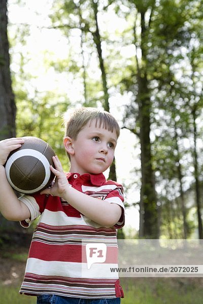 Ein kleiner Junge steht auf einer Wiese mit einem Football in der Hand