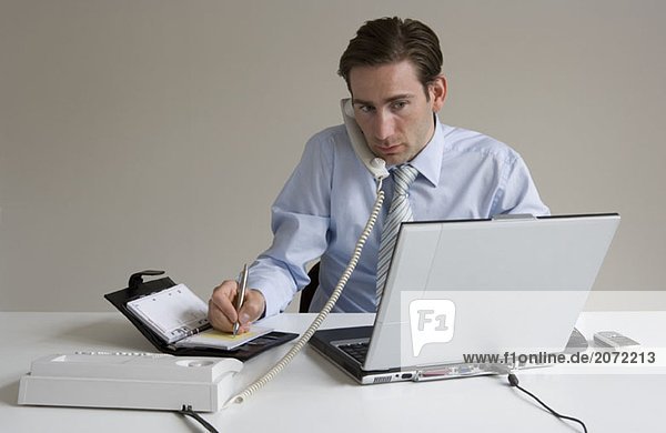 Ein telefonierender Geschäftsmann arbeitet am Laptop und notiert Termine in einen Timer